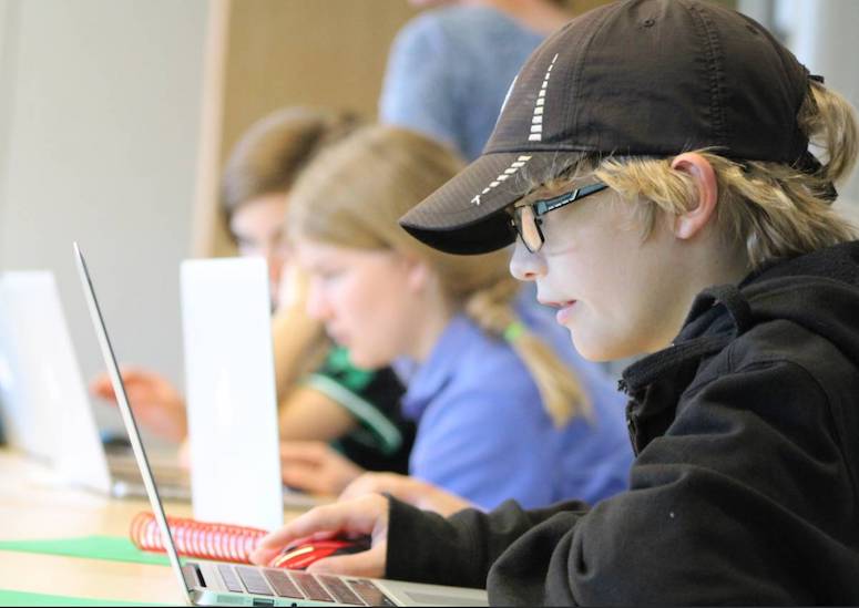 Profile view of three children sitting at their laptops coding.