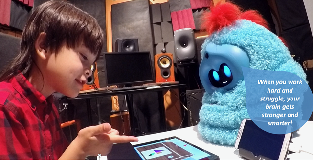 A child completes a task on a tablet while a fluffy blue Tega robot tells him, 'When you work hard and struggle, your brain gets stronger and smarter!'