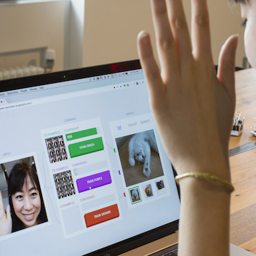 A woman waves at her laptop screen as she uses the Teachable Machines platform to train a classifier